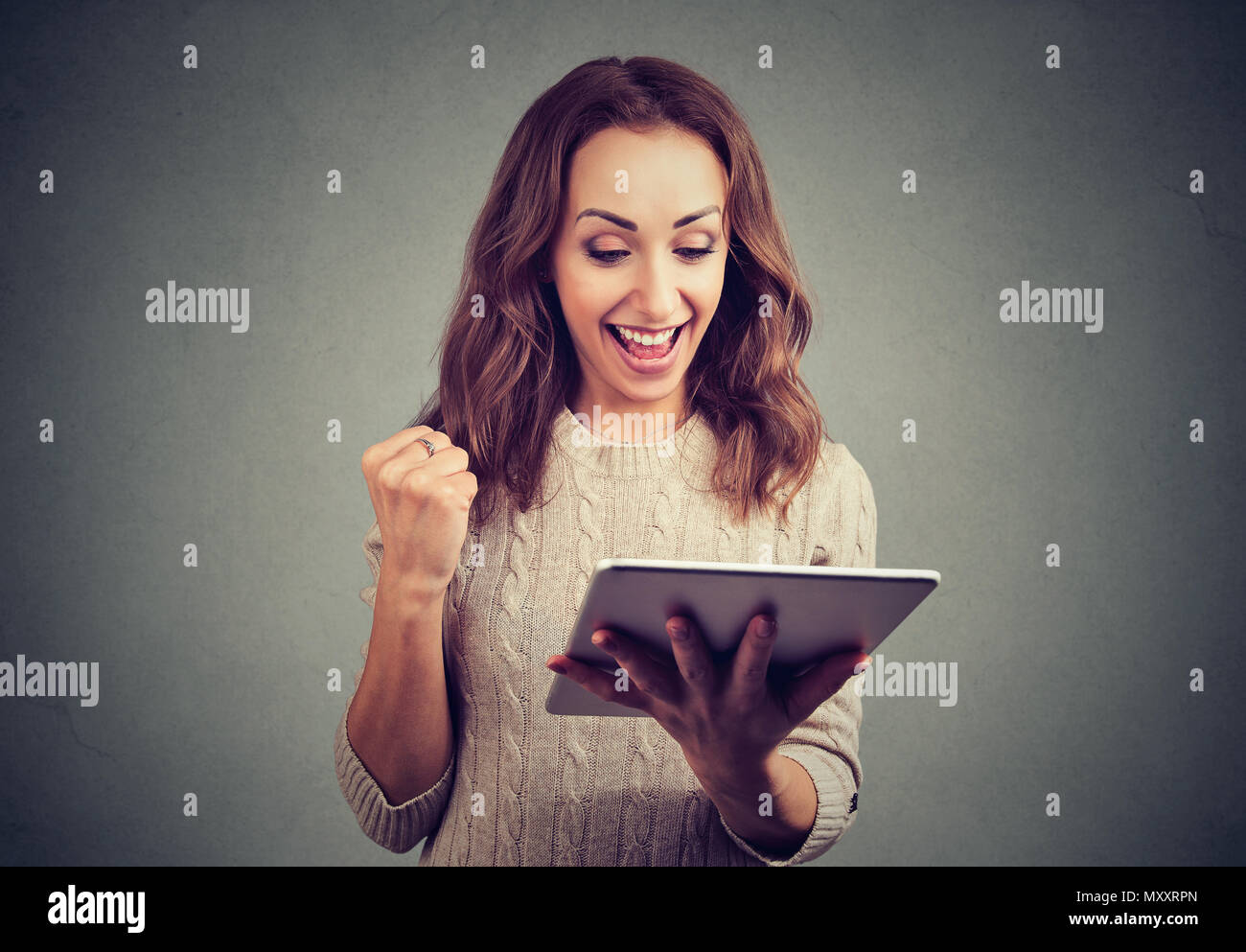 Freundliche nette Frau in holding Faust mit Erfolg glücklich, während sie Tablet auf grauem Hintergrund. Stockfoto