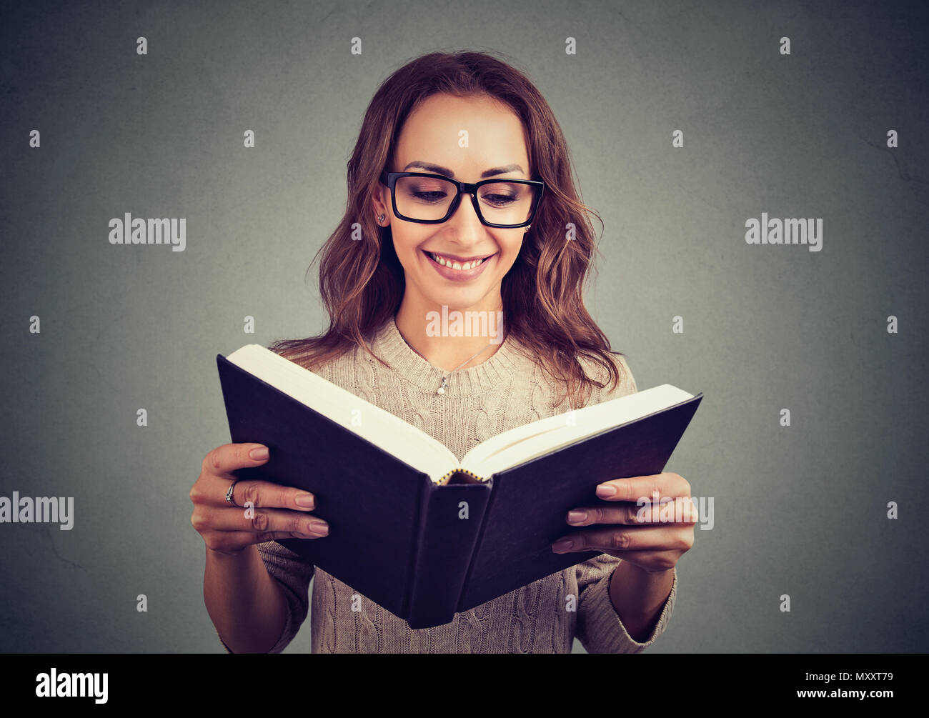 Ziemlich Casual Mädchen in Gläsern mit interessanten Buch lesen auf grauem Hintergrund Stockfoto