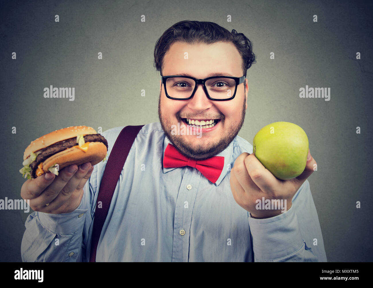 Glückliche junge chunky Mann mit grünen frischen Apfel und Hamburger Wahl und lächelnd an Kamera Stockfoto