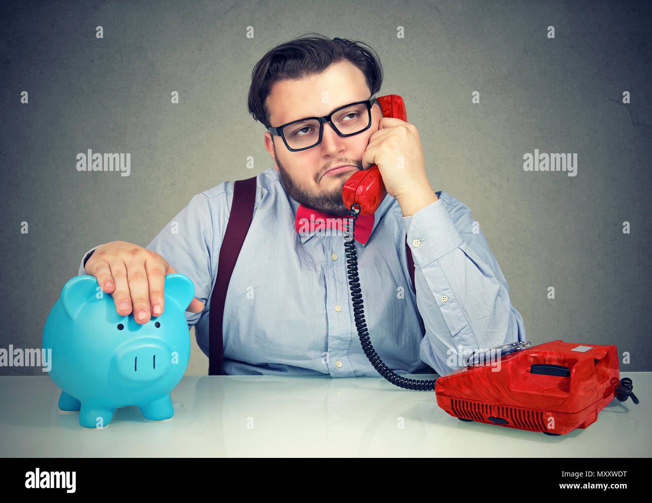 Chubby business Mann sitzt mit sparschwein bei Tisch und in dumpfen Telefongespräch suchen genervt Stockfoto