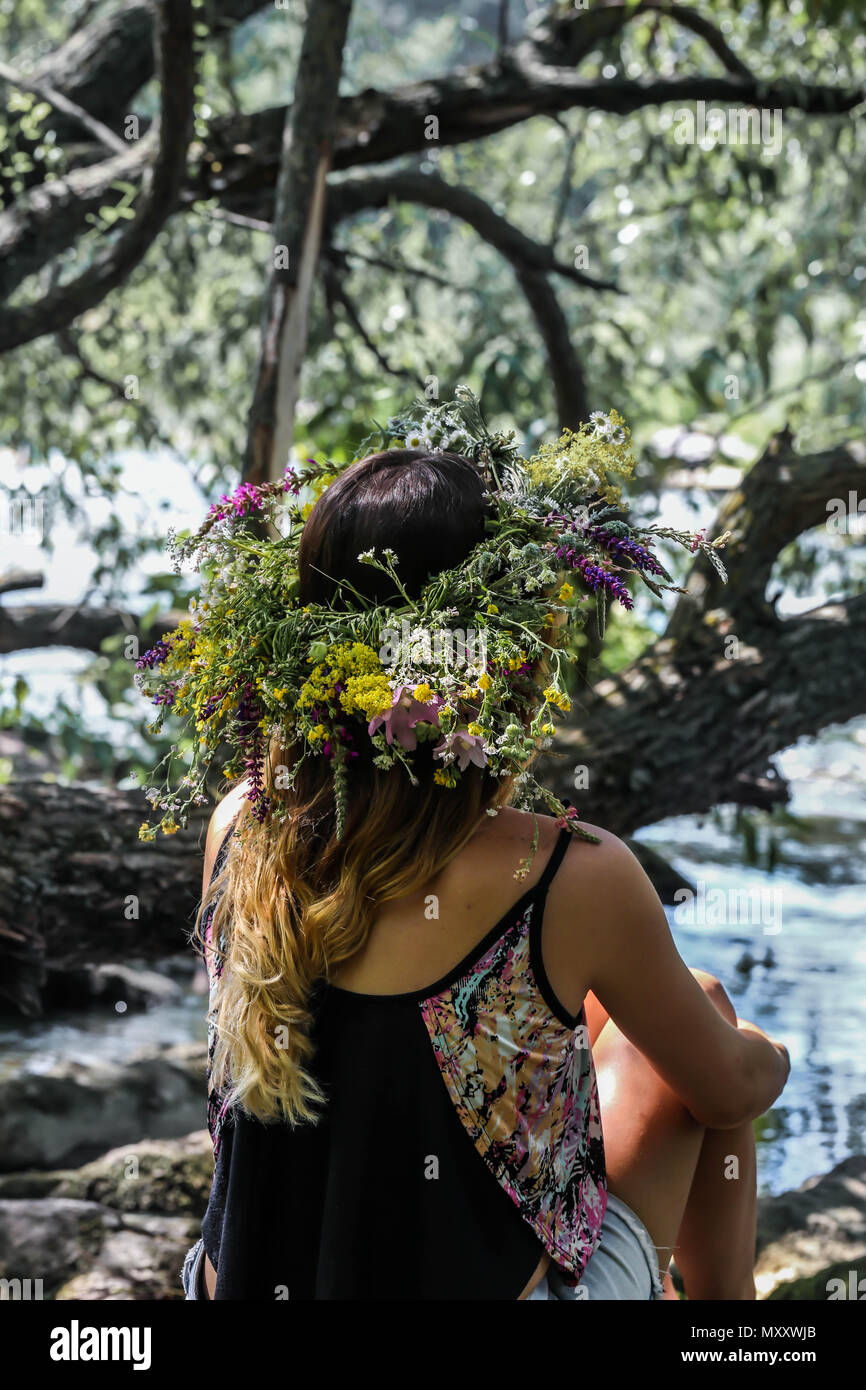 Schöne Mädchen in einem Kranz von Blumen am Ufer des Flusses, an einem sonnigen Tag. Die heidnischen Ritus eines jungen Mädchens von der Sonnenwende. Tag der Erde Stockfoto