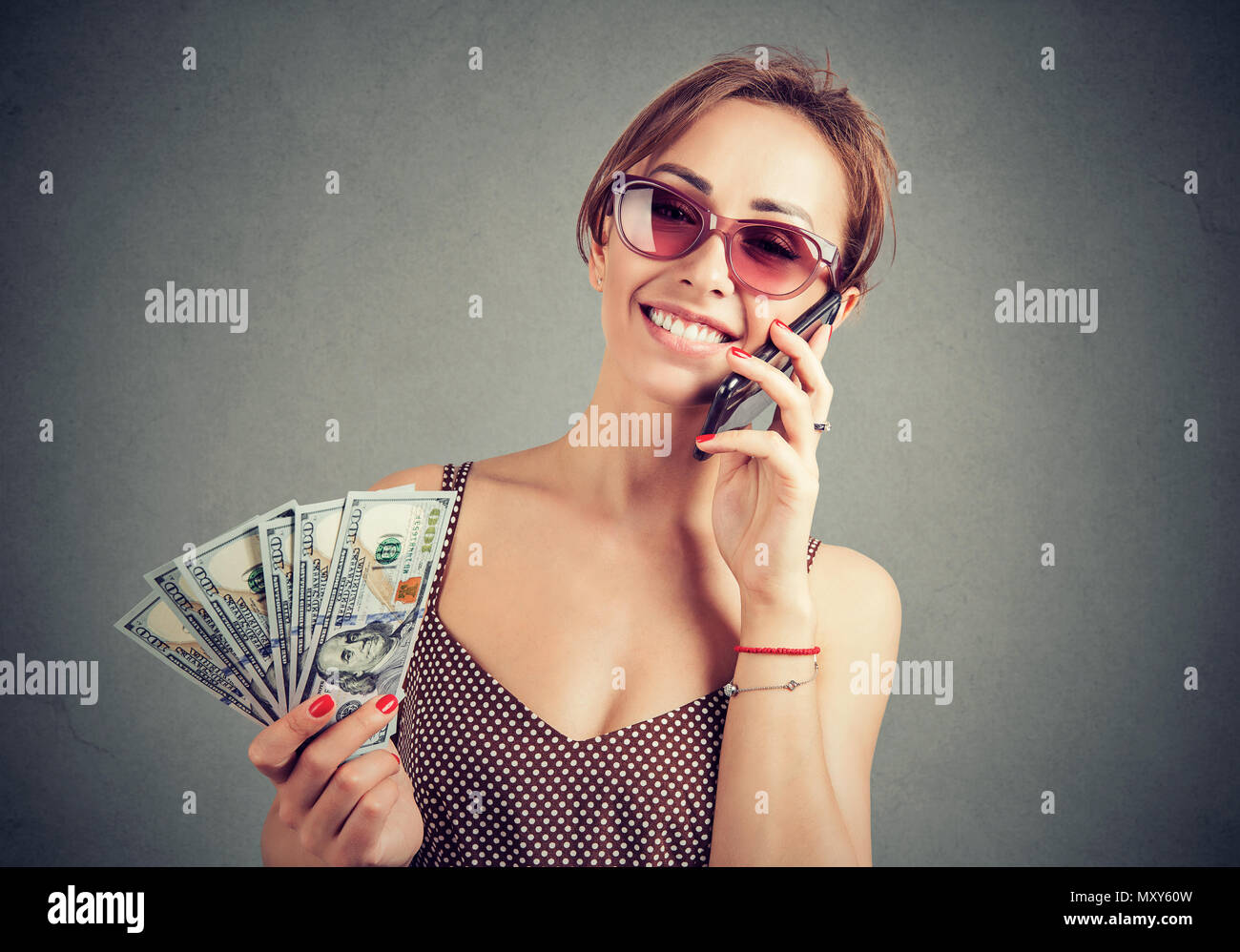 Stilvolle Frau in Sonnenbrille holding Haufen von Dollar und sprechen auf dem Smartphone Suche erfolgreich. Stockfoto