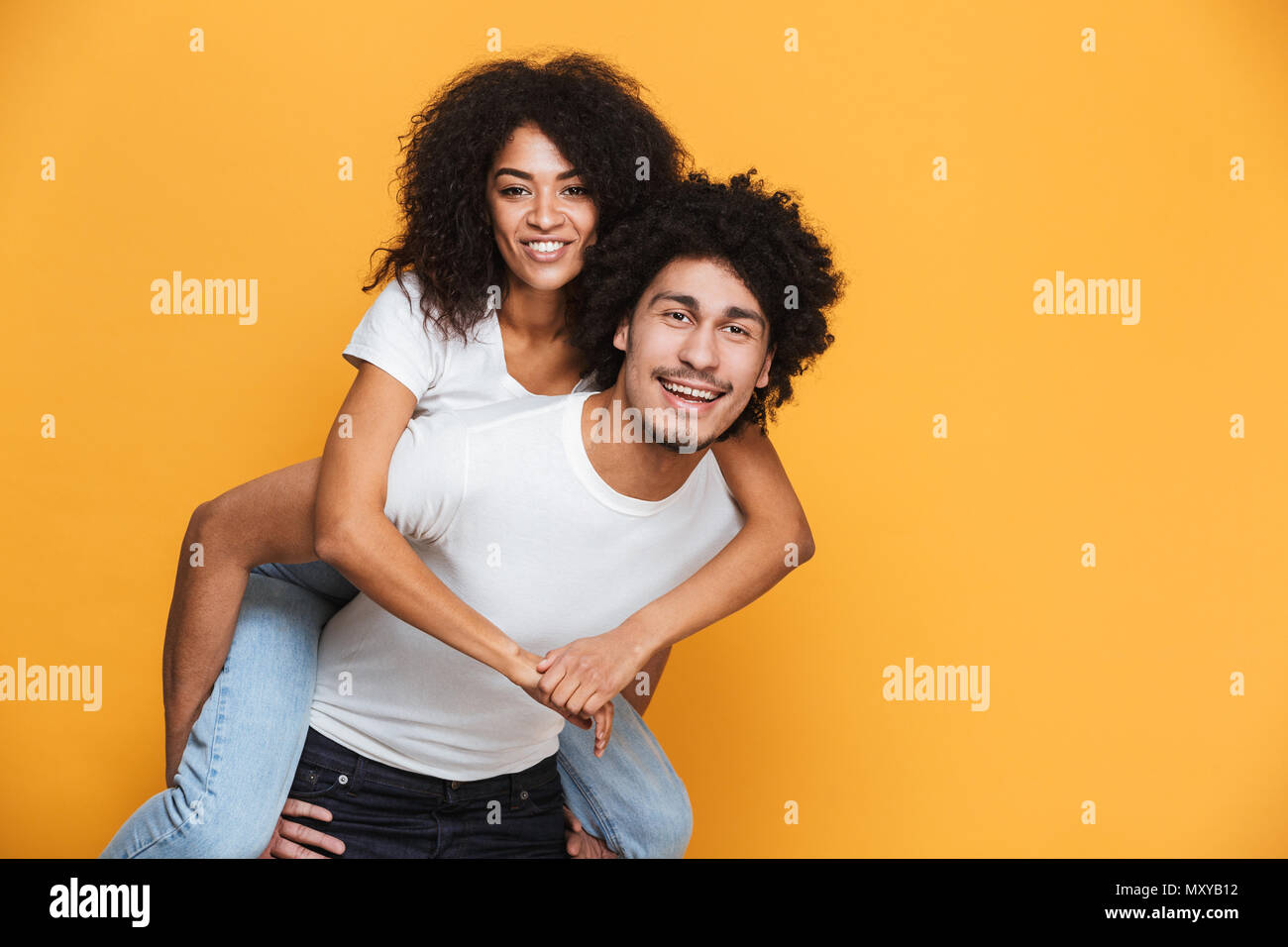 Porträt eines lächelnden afrikanischen Mann, Freundin auf seinem Rücken über Gelb Hintergrund isoliert Stockfoto