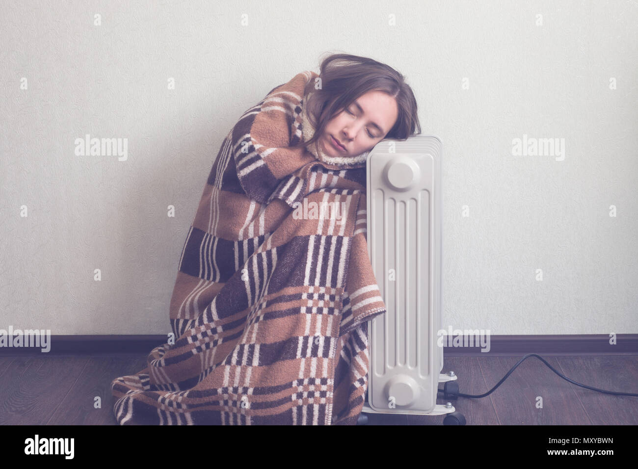 Junge Frau in der Wolldecke plaid Warm up Hände über elektrische Heizung Stockfoto