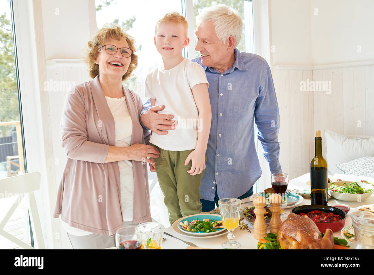 Portrait des modernen älterer Mann und Frau posiert mit kleinen Enkel stehen Tisch und glücklich lächelnd in die Kamera, kopieren Raum Stockfoto