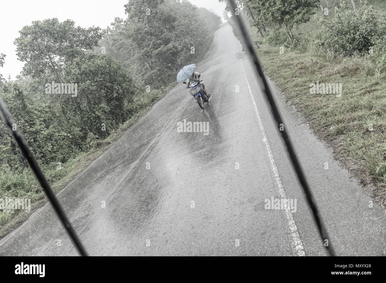 Motorradfahrer gefangen in einer Regendusche, Kanchanaburi, Thailand Stockfoto