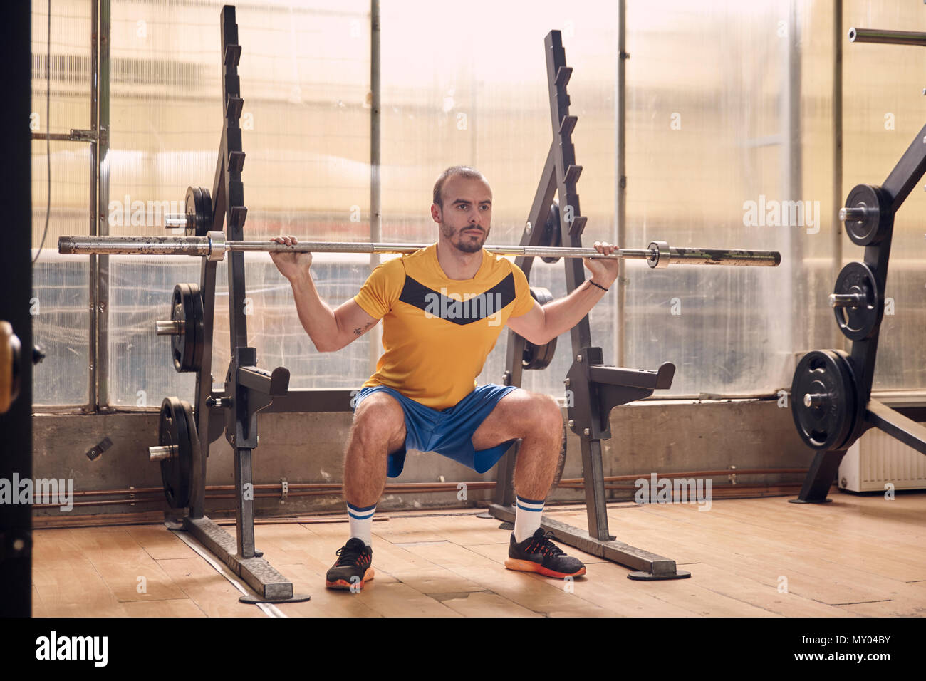 Ein junger Mann, tragen sportliche Kleidung, Hocke Übung mit Bar, in der Altstadt verprügelt Fitnessraum Interieur. voller Länge geschossen. Stockfoto