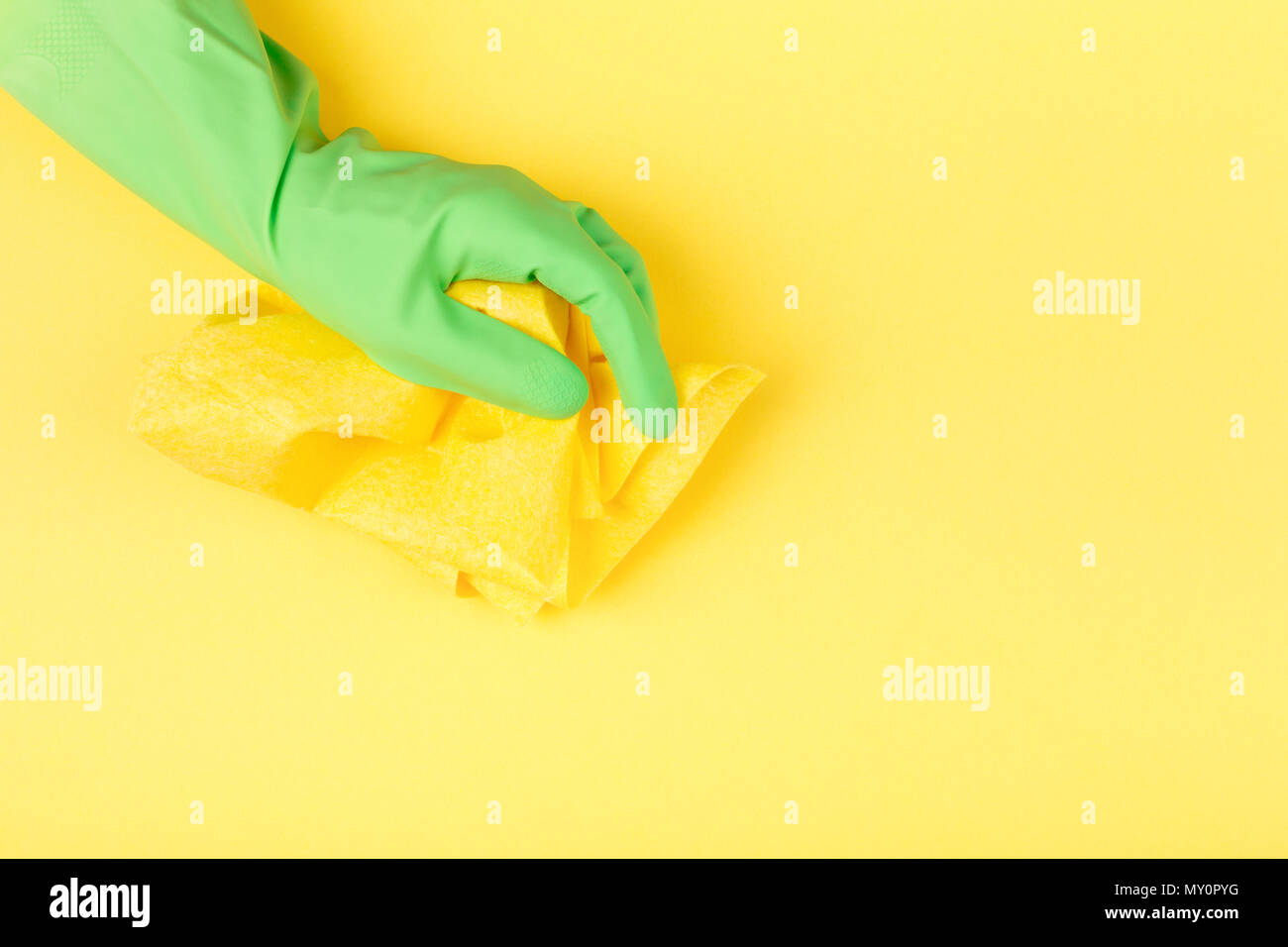 Hand in grün Gummi Schutzhandschuh mit gelben Lappen auf gelben Hintergrund. Reinigung Konzept. Stockfoto