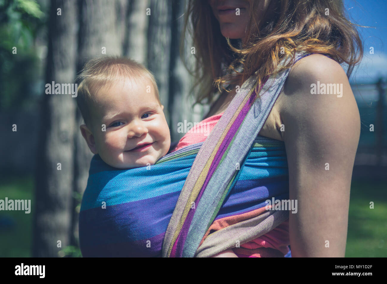 Eine junge Mutter ist draußen stehen, mit ihrem Baby im Tragetuch Stockfoto