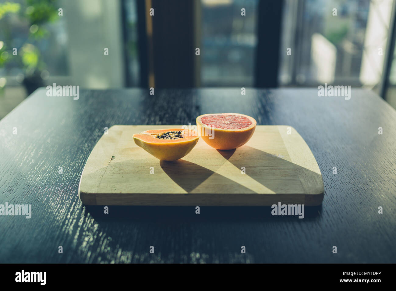 Eine Grapefruit und eine Papaya auf ein Schneidebrett in der Morgensonne Stockfoto