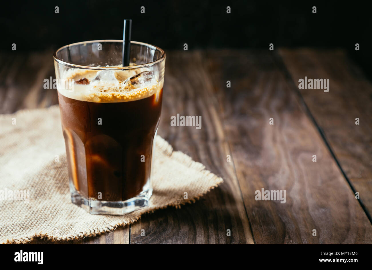 Schwarz Eiskaffee in einem hohen Glas mit einem Stroh auf einem rustikalen Holztisch Stockfoto