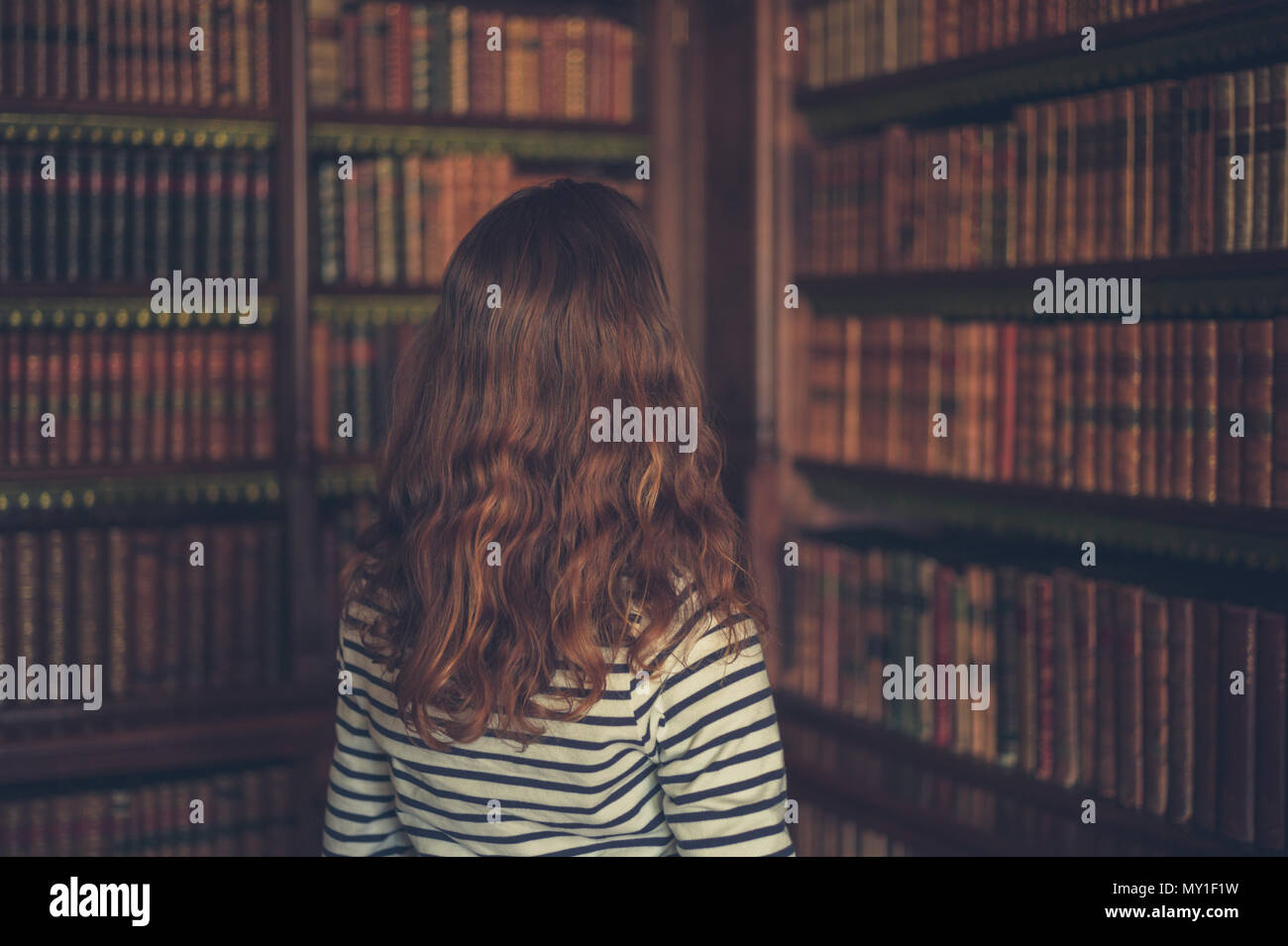 Eine junge Frau schaut sich die Bücher auf den Regalen in eine alte Bibliothek Stockfoto