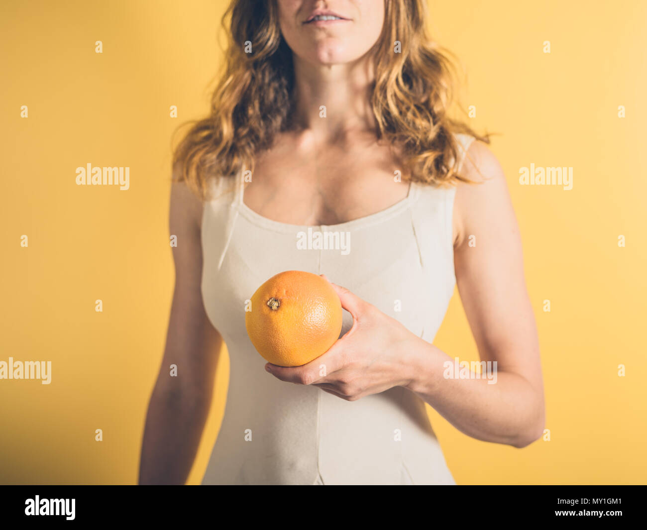 Eine junge Frau steht vor einem gelben Hintergrund Holding eine Grapefruit Stockfoto