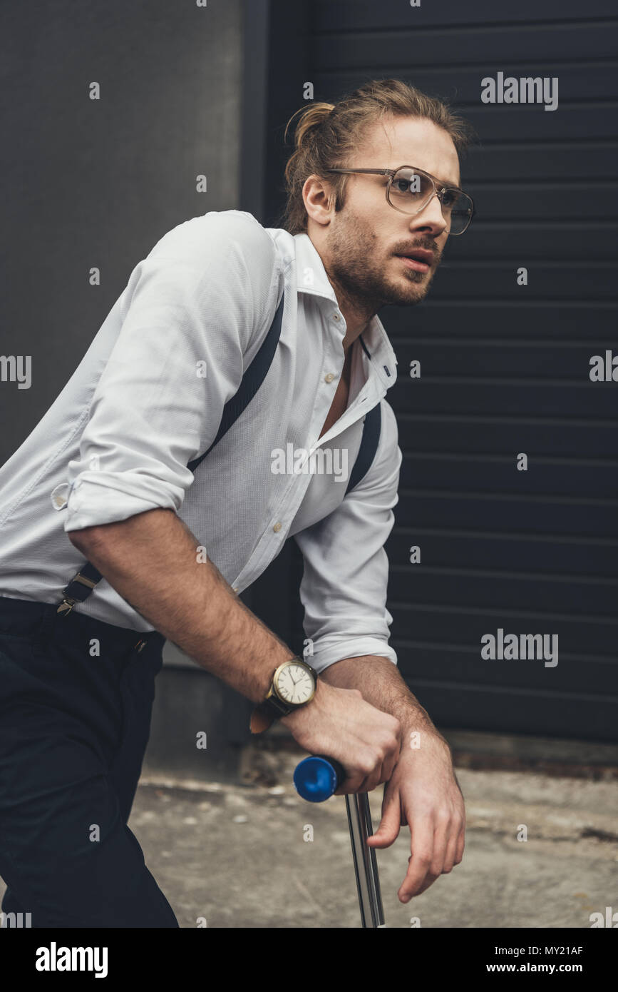 Stilvolle bärtiger junger Mann in Brillen stehen auf Roller und Wegsehen Stockfoto