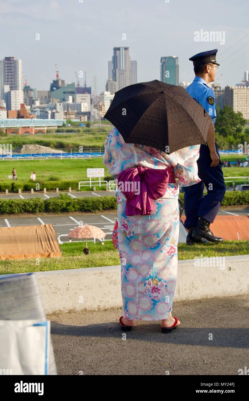 Eine japanische Frau trägt eine traditionelle bunte Yukata mit Blumen und einen Regenschirm als Sonnenschutz bei einem Sommer Matsuri Festival in Osaka Stockfoto