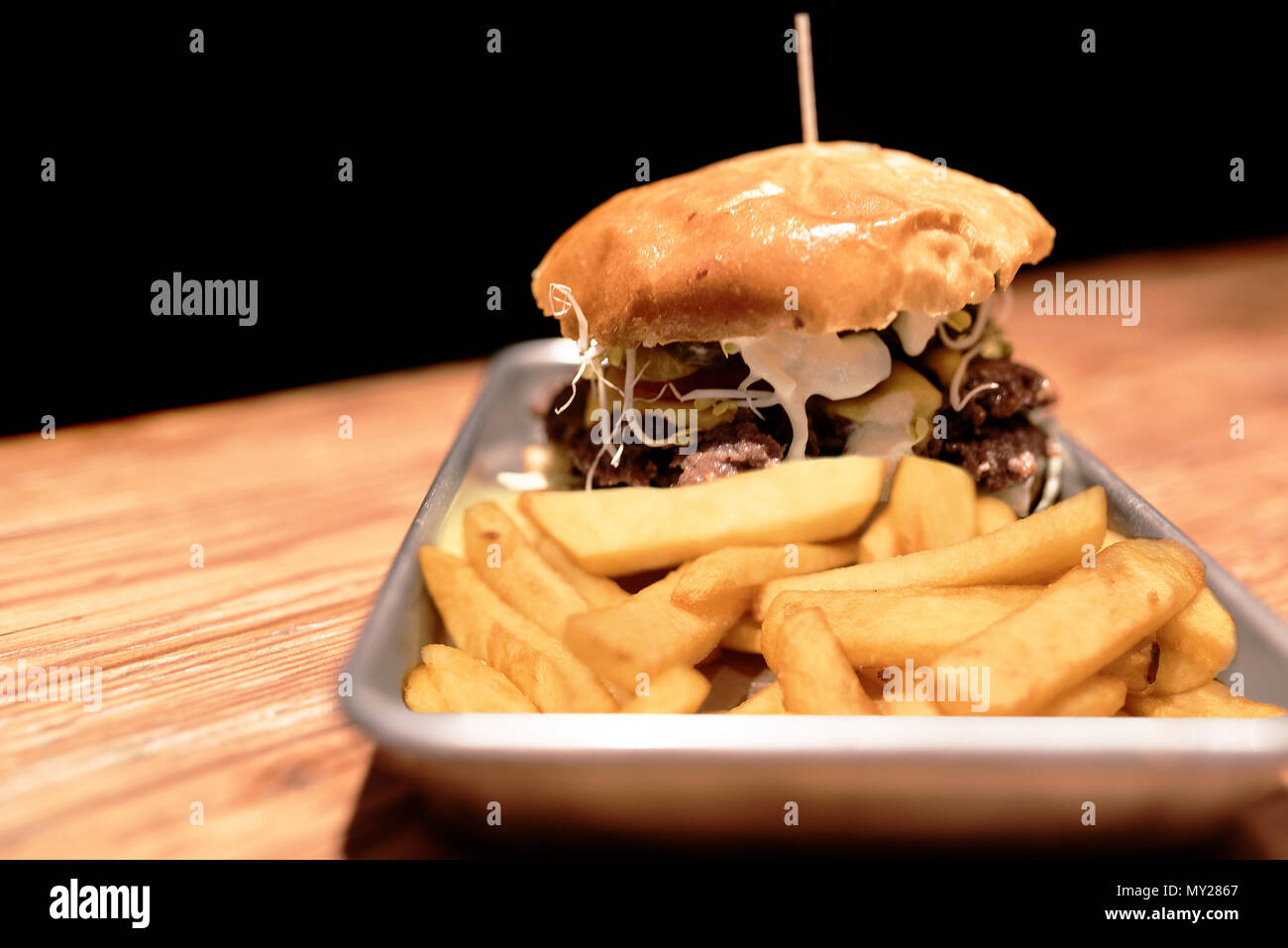 Große Burger und Pommes frites auf Metallplatte auf rustikalen Holztisch gegen den dunklen Hintergrund Stockfoto