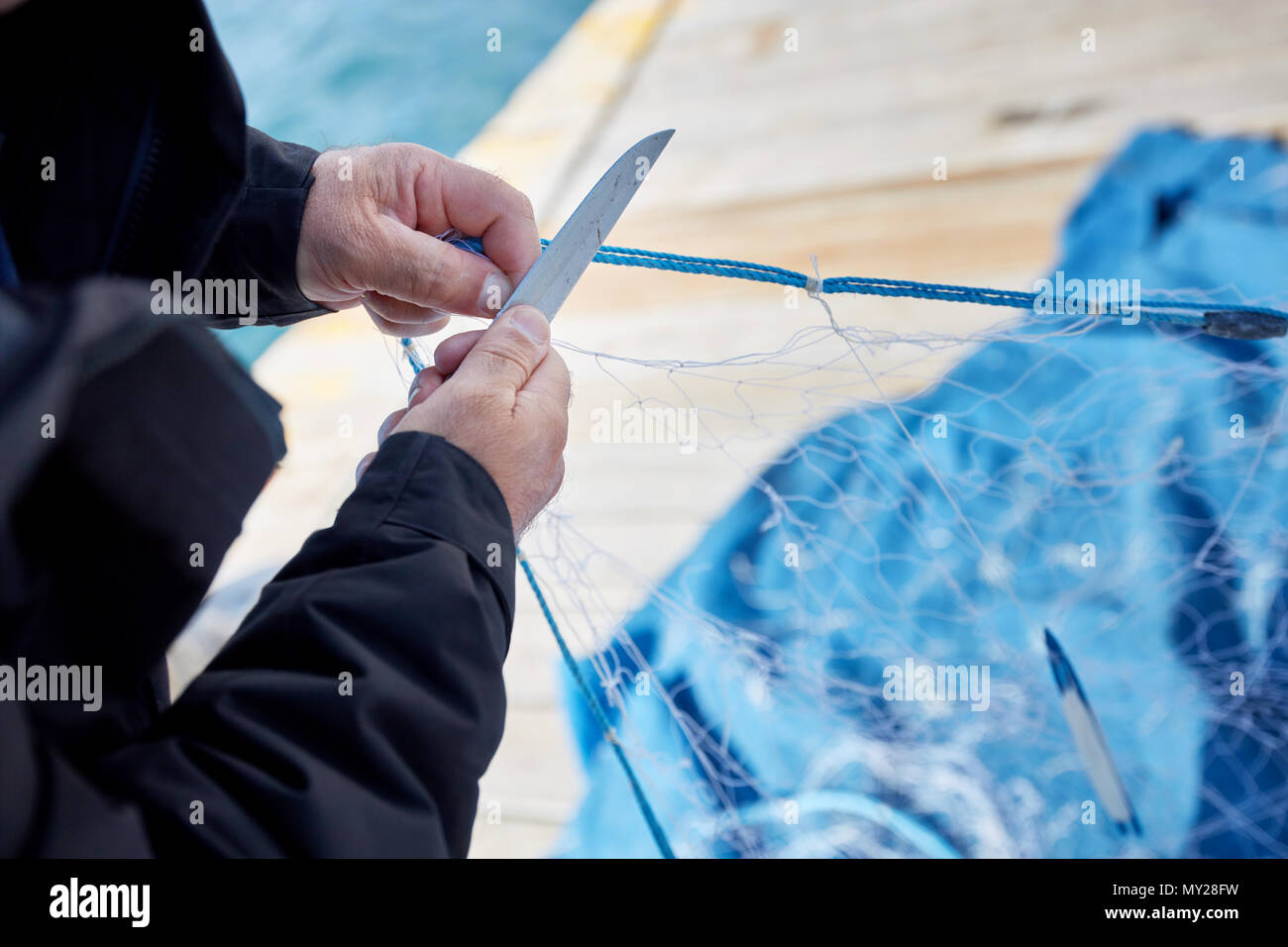 Fischer Instandsetzung ein Fischerdorf, das Netz mit einem Messer auf den Hafen Stockfoto