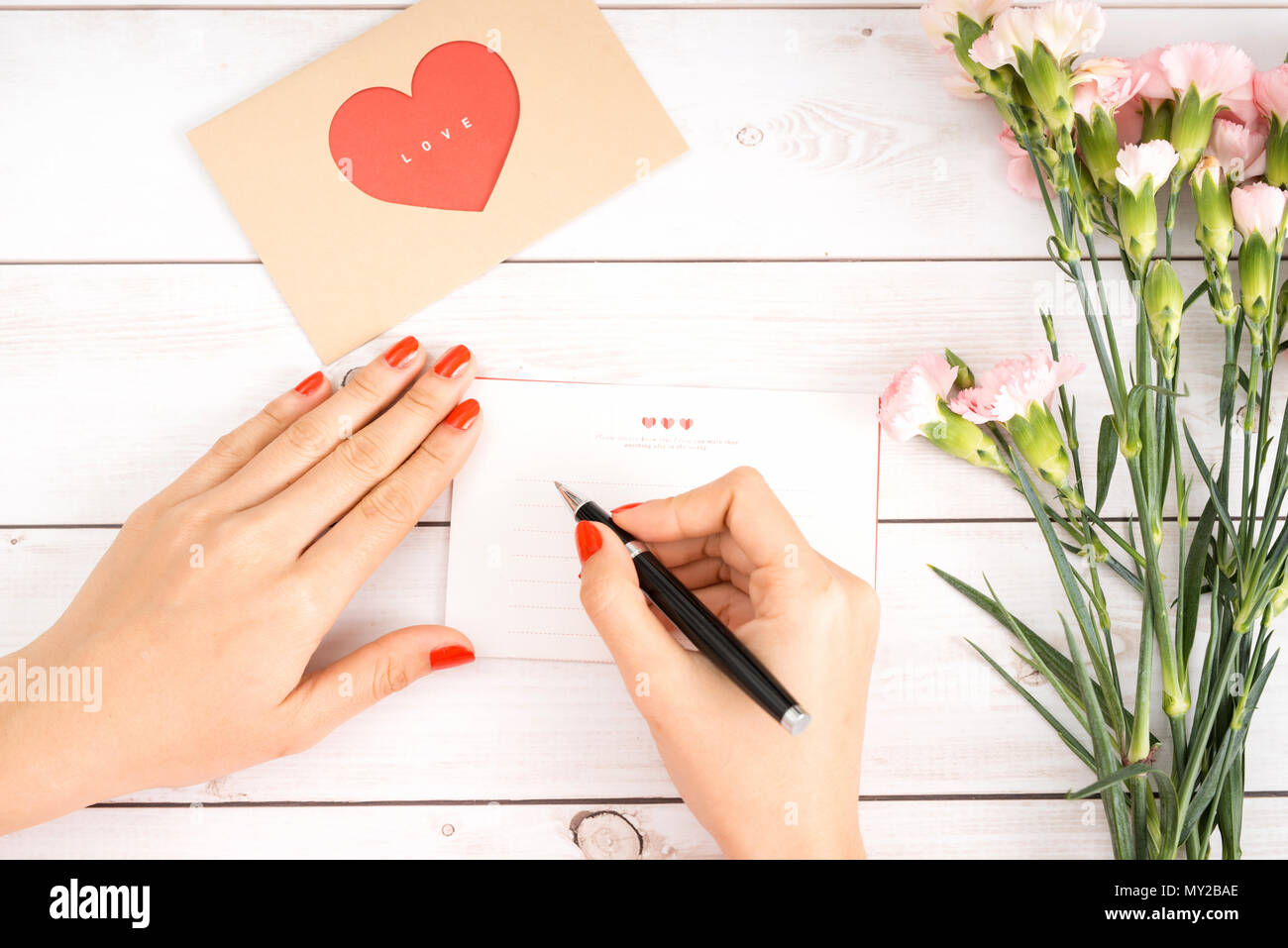 Frau schreibt Liebesbrief auf weißem Papier mit roten Herzen Form zahlen. Hand Postkarte für Saint Valentines Tag Feier gemacht. Schicken sie Briefe für Ihren lov Stockfoto