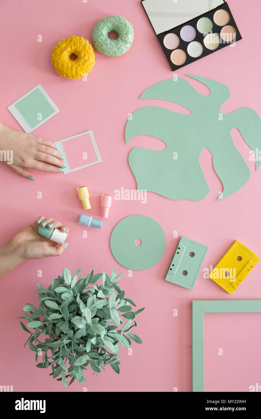 Frau mit grünen Nagellack am Schreibtisch mit Donuts, Make-up Palette, gelbe Kassette und Anlage Stockfoto