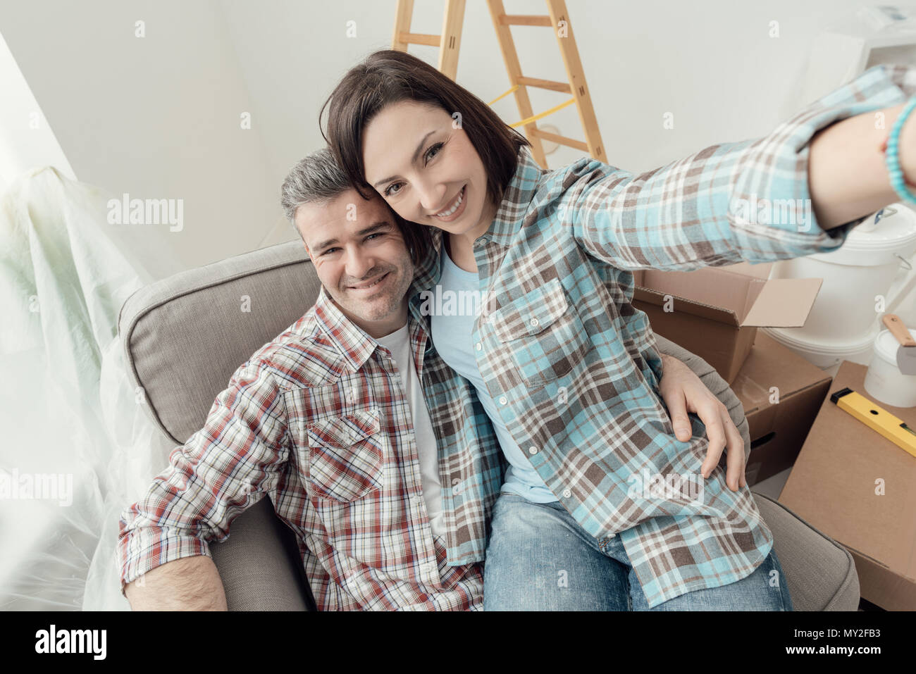 Glückliches Paar unter selfies zu Hause, während sie Haupterneuerungen, Sie sitzen auf einem Sessel und lächelnd Stockfoto