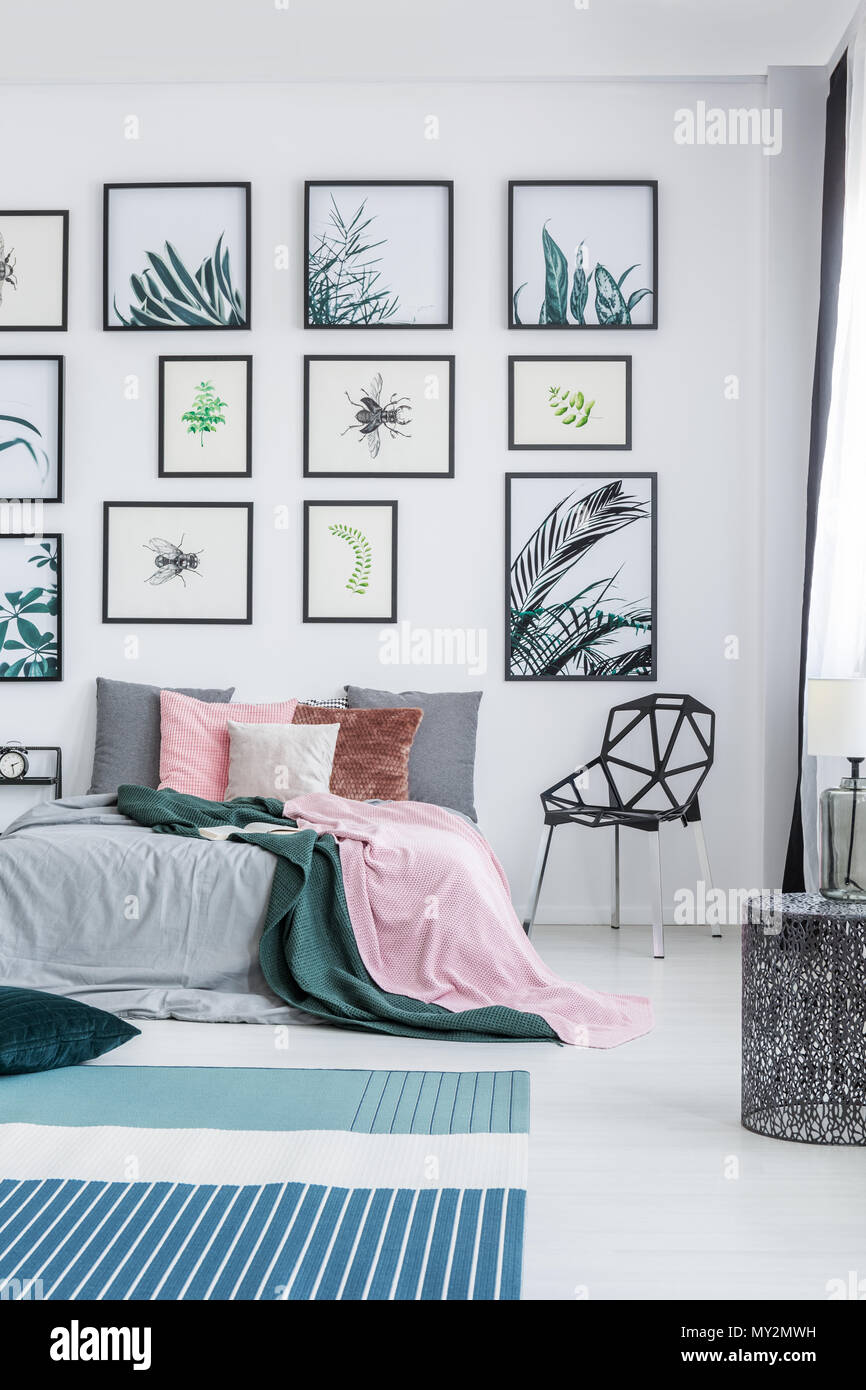Real Photo von einem breiten Bett steht neben einem schwarzen Stuhl in  einem Schlafzimmer Einrichtung mit Pflanzen Poster an der Wand und  Teppichen auf dem Boden Stockfotografie - Alamy