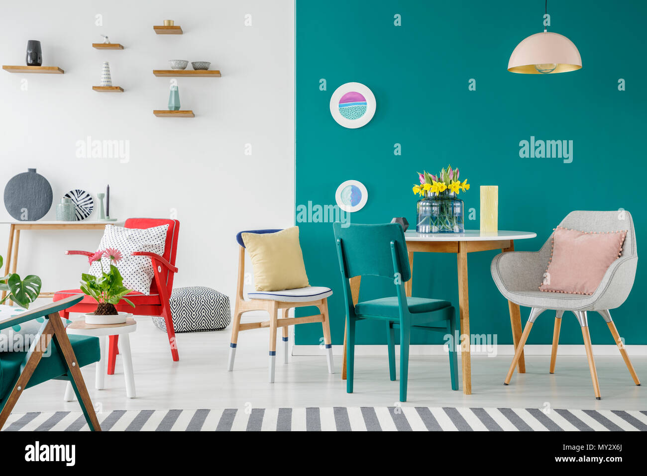 Stühle an den hölzernen Tisch gegen grüne Wand in bunten Wohnung Interieur mit Blumen Stockfoto