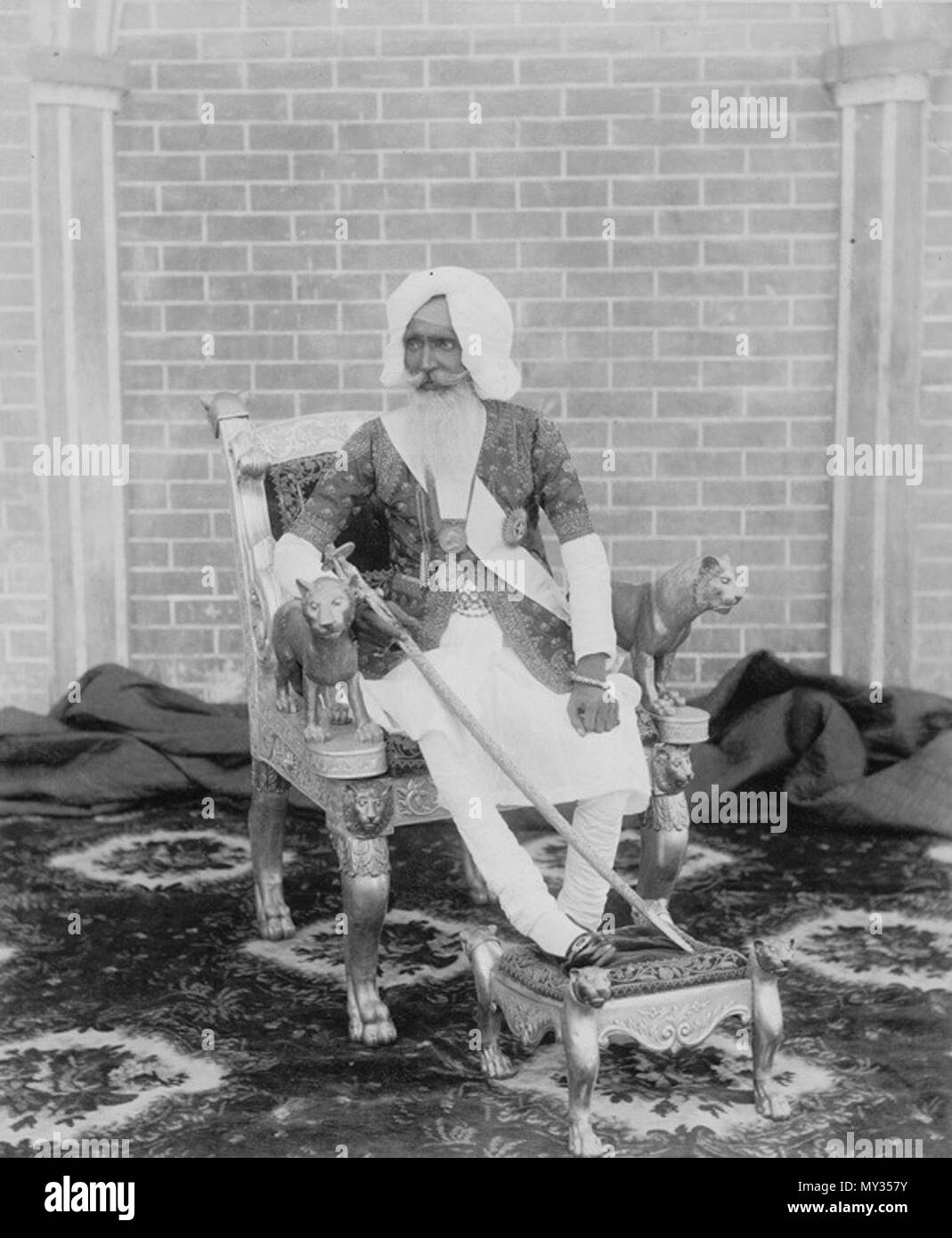 . Englisch: Foto von Sir Hira Singh, der Raja von Nabha, von einem unbekannten Fotografen in den 1890er Jahren genommen. Diese in voller Länge Porträt zeigt die Raja sitzt auf einem vergoldeten Thron mit seinem rechten Bein auf einen Hocker. Er ist in den königlichen Insignien inklusive Medaillen und halten ein Juwel - verkrustete Schwert gekleidet. Die Arme der Thron von geschnitzten Löwen gebildet. Der Raja (1843-1911) regierte die fürstlichen Zustand von nabha im Punjab von 1871 bis zu seinem Tod. Ein Sikh, er war ein Mitglied der Phulkian Dynastie gingen vom Sidhu Jats. Familien der Dynastie Patiala, Feudalstaat, Nabha, Bahadur und andere Punjab Stockfoto