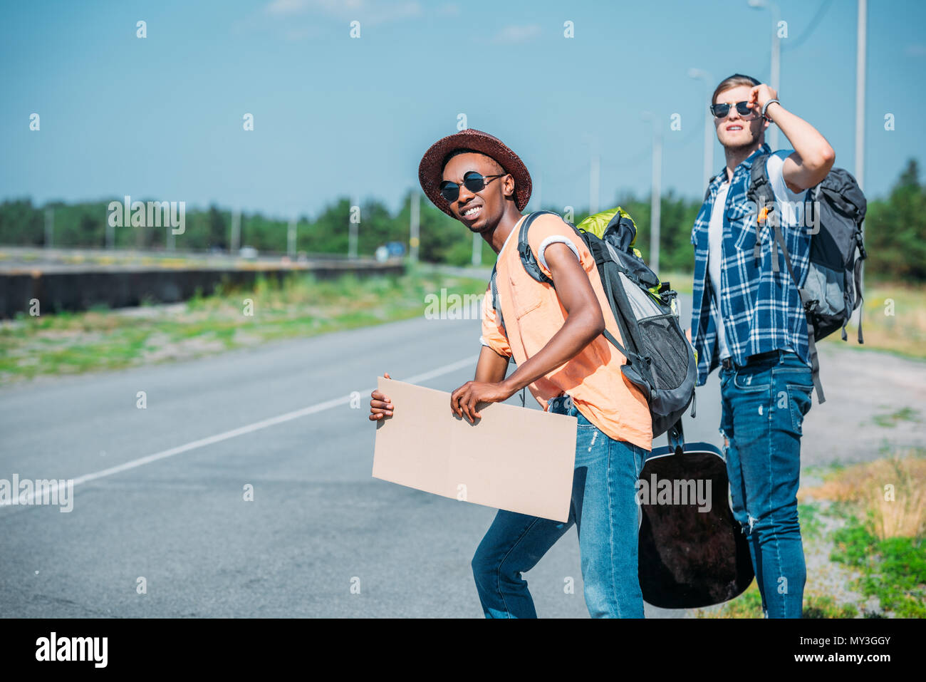 Multiethnischen junge Männer mit leeren Karton auf der Suche nach Auto beim Trampen während der Reise Stockfoto