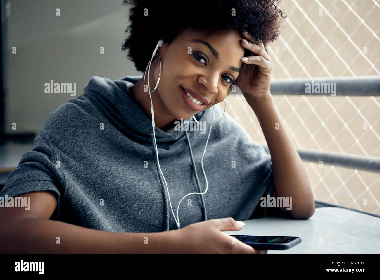 Junge Frau mit Smartphone- und Ohrhörer, Lächeln, Porträt Stockfoto