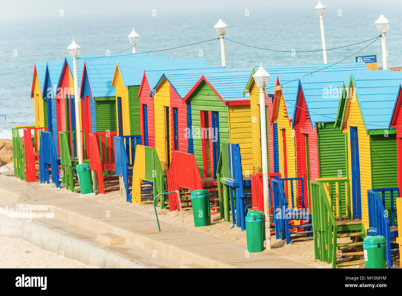 Bunte Badehäuschen in einer Reihe am weißen Sandstrand von Muizenberg unter einem blauen Sommerhimmel. Muizenberg, Kapstadt, Südafrika. Stockfoto