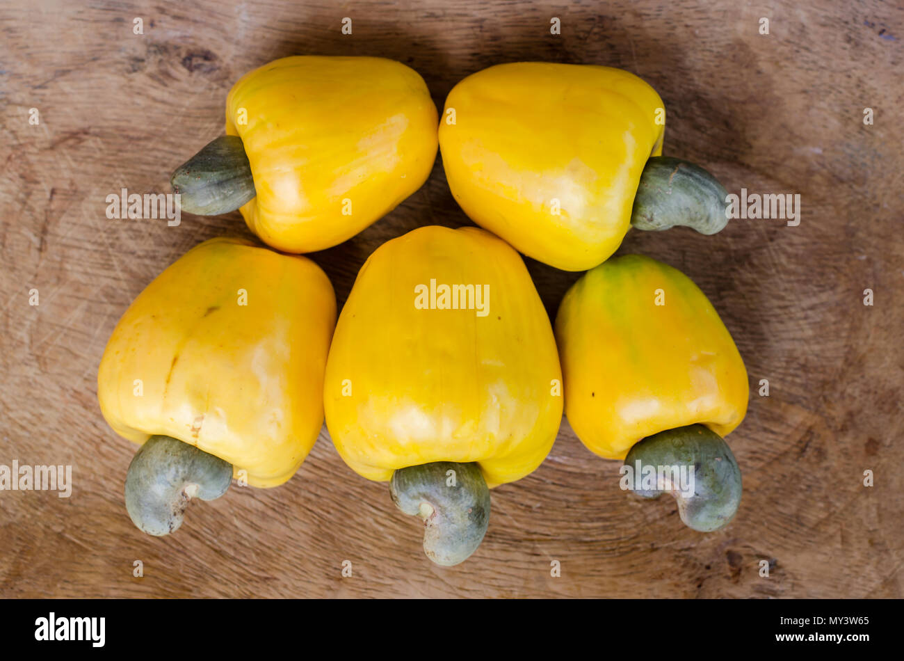 Frisch gepflückte gelbe Cashew-Früchte auf einem rustikalen Holztisch, die ihre lebhafte Farbe und natürliche Schönheit zeigen. Stockfoto