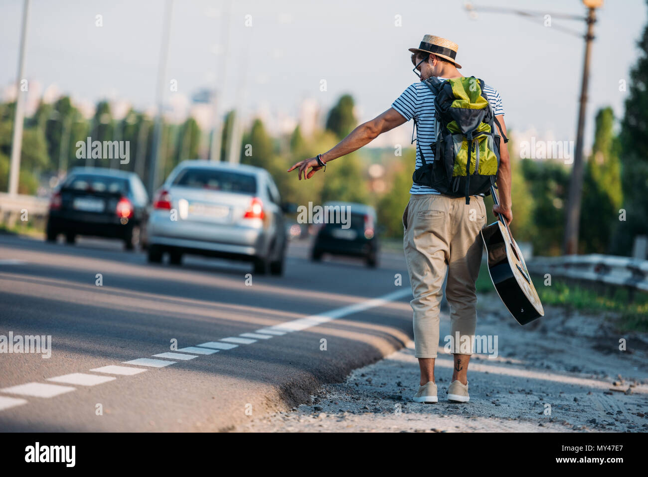 Rückansicht des jungen Mann mit Gitarre Gestik Auto alleine per Anhalter zu stoppen Stockfoto