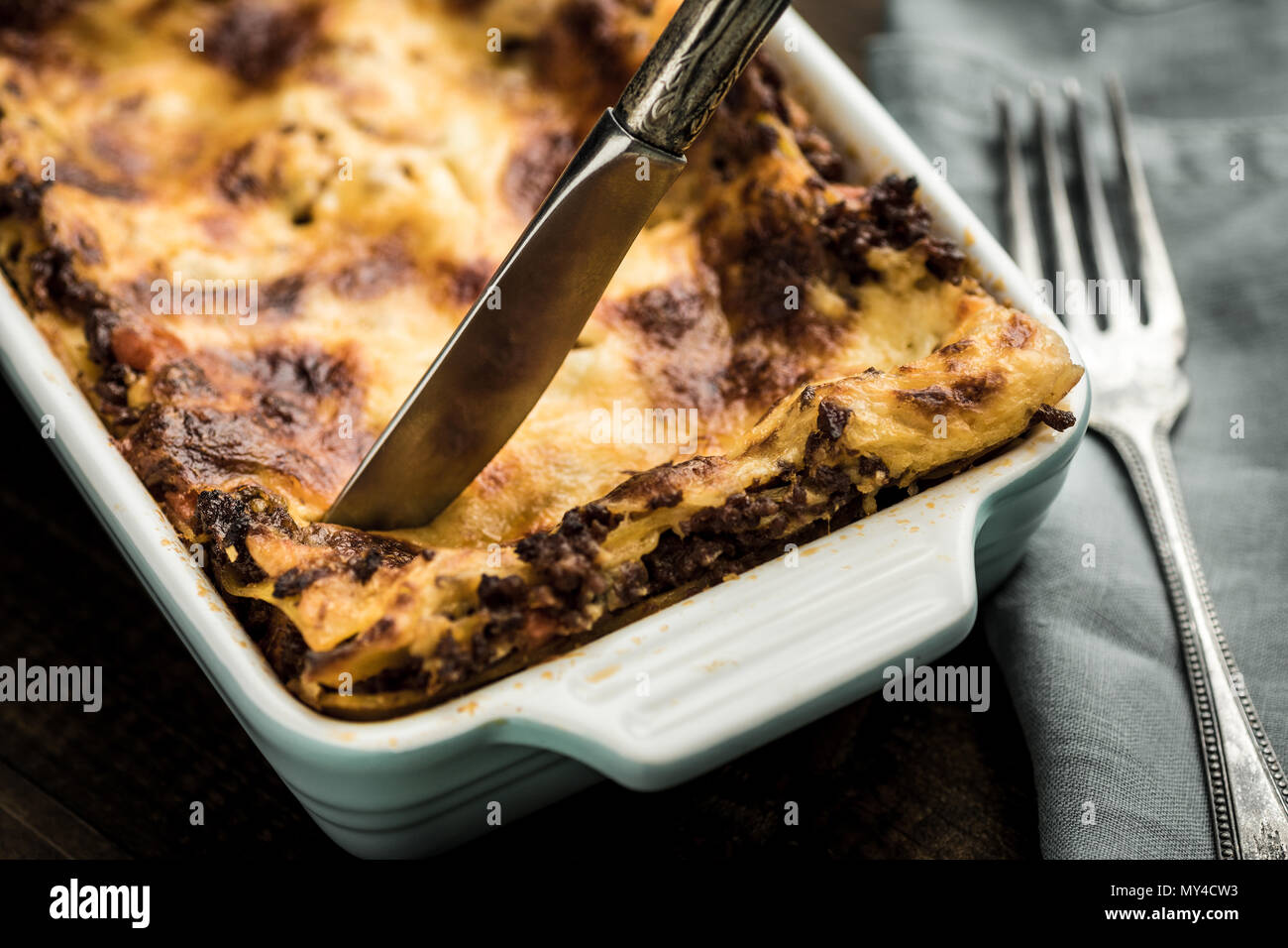 Messer schneidet Lasagne auf dunklen Holztisch Stockfoto