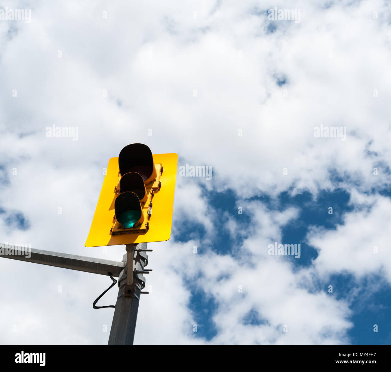 Ampel auf Metall Pol mit grünes Licht leuchtet in gelb Struktur gegen teilweise bewölktem Himmel. Stockfoto