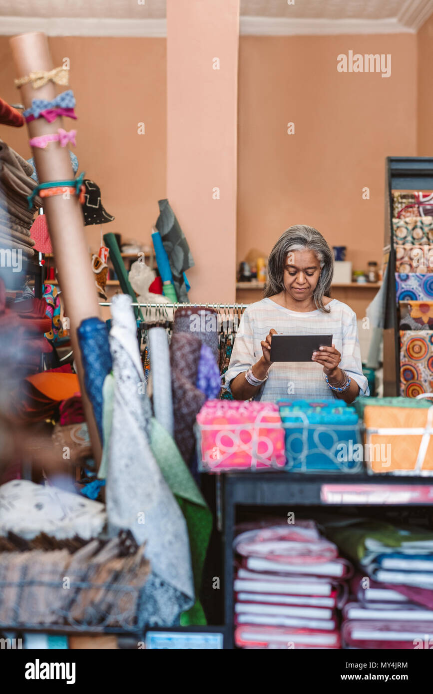 Reifen Stoff shop besitzer mit einem digitalen Tablet steht hinter einem Zähler von bunten Tüchern und Textilien umgeben Stockfoto