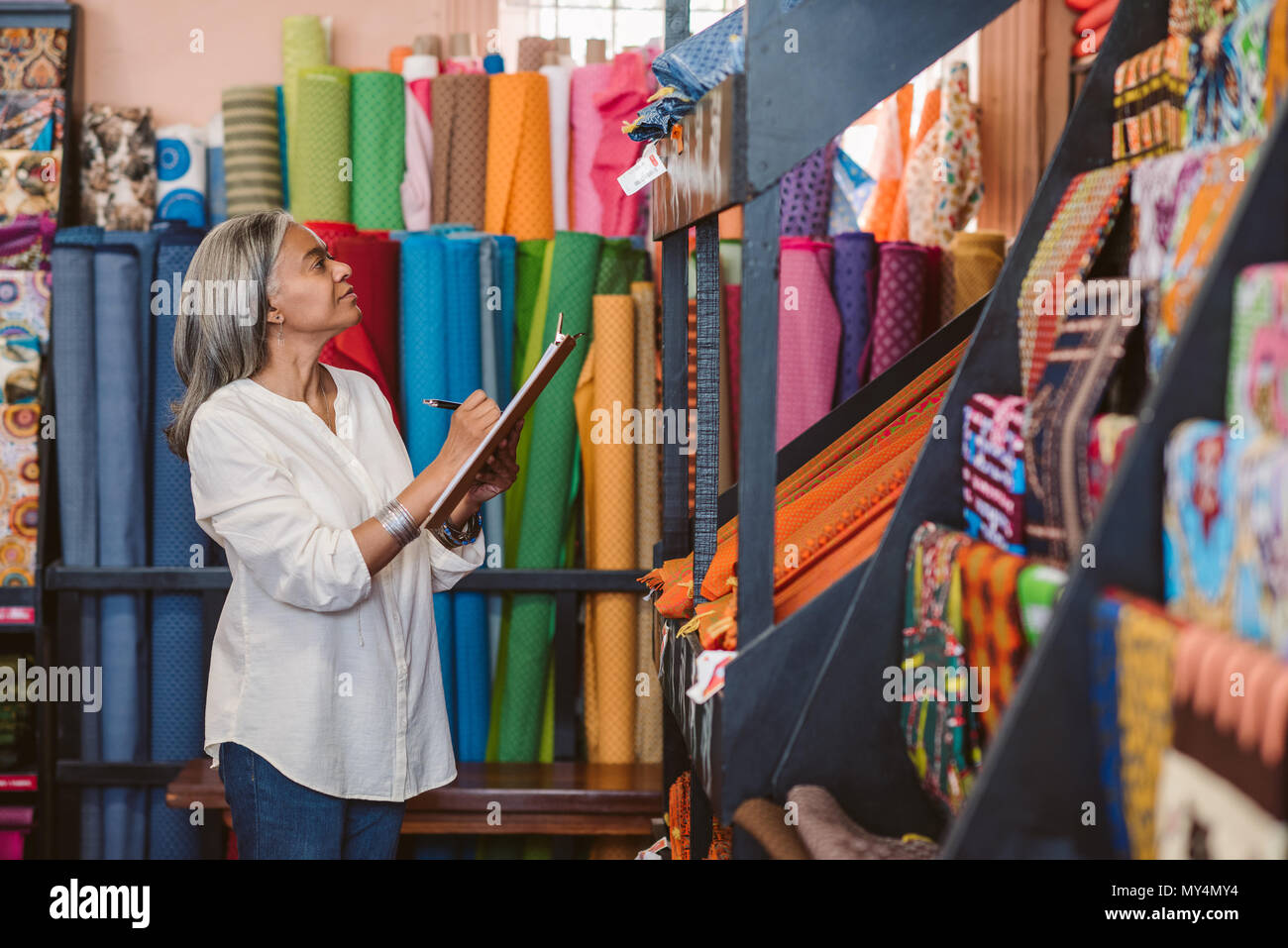 Reifen fabric store Inhaber stehen in Ihrem Shop von bunten Tüchern und Textilien Bestandsaufnahme mit einem Klemmbrett umgeben Stockfoto