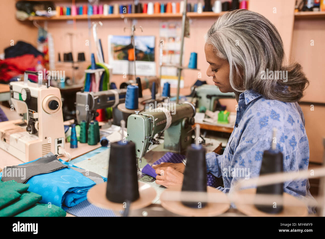 Reifen Näherin sitzt an einer Nähmaschine nähen ein Stück bunten Stoff während der Arbeit allein in ihrer Kleidung workshop Stockfoto