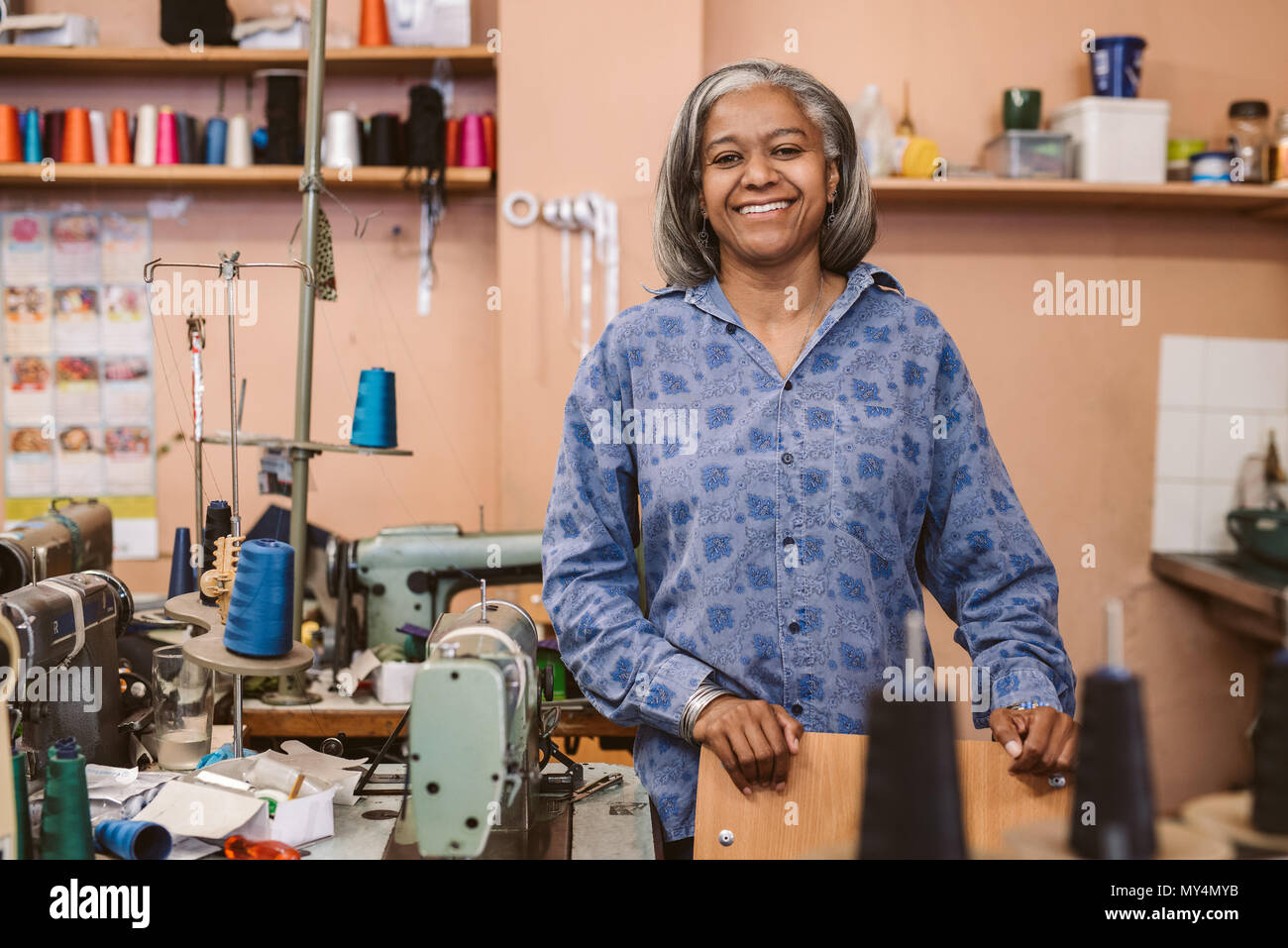 Porträt eines lächelnden reife Näherin, um einen Tisch in Ihrem Gewebe workshop umgeben von nähtechnik Stockfoto