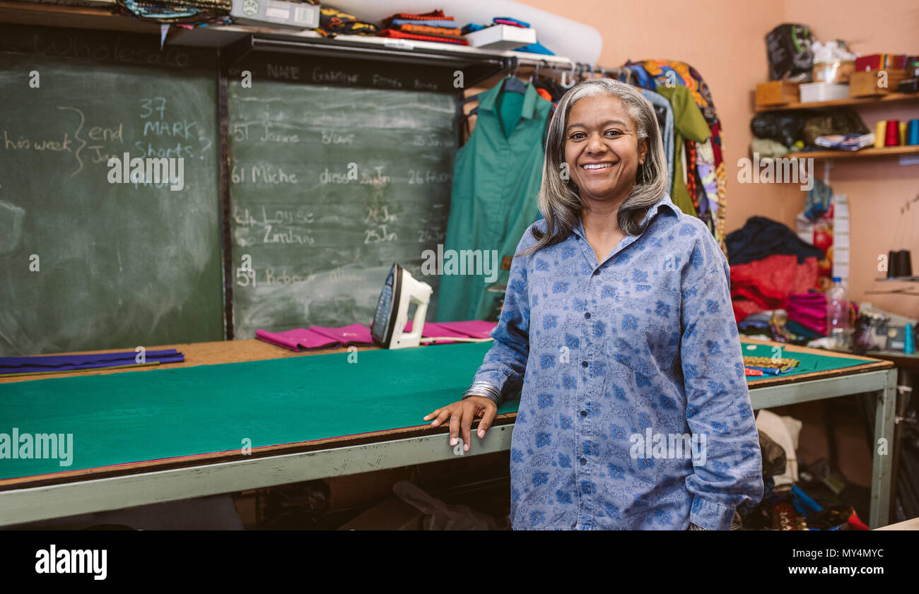 Porträt eines lächelnden reife Näherin, um einen Tisch in Ihrem Gewebe workshop umgeben von nähtechnik Stockfoto