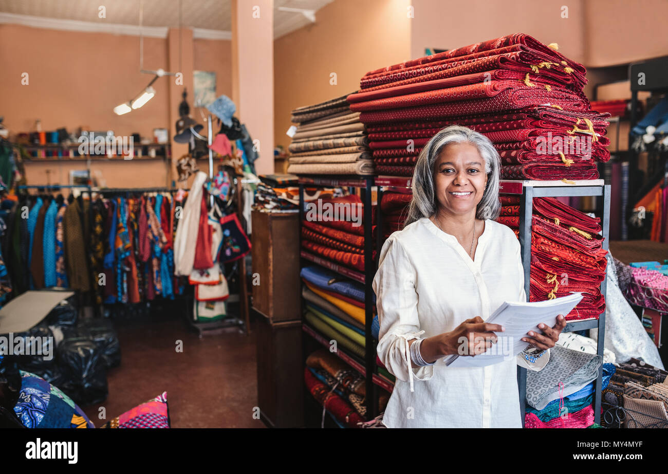 Porträt eines lächelnden reife Stoff shop besitzer lesen Papierkram beim Stehen neben Regale voll von bunten Tüchern und Textilien Stockfoto
