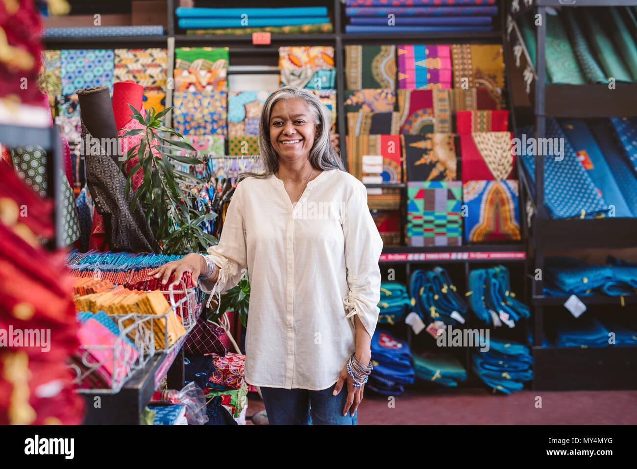 Porträt eines lächelnden reife Stoff shop besitzer stehen Racks und Regale voll von bunten Tüchern und Textilien Stockfoto