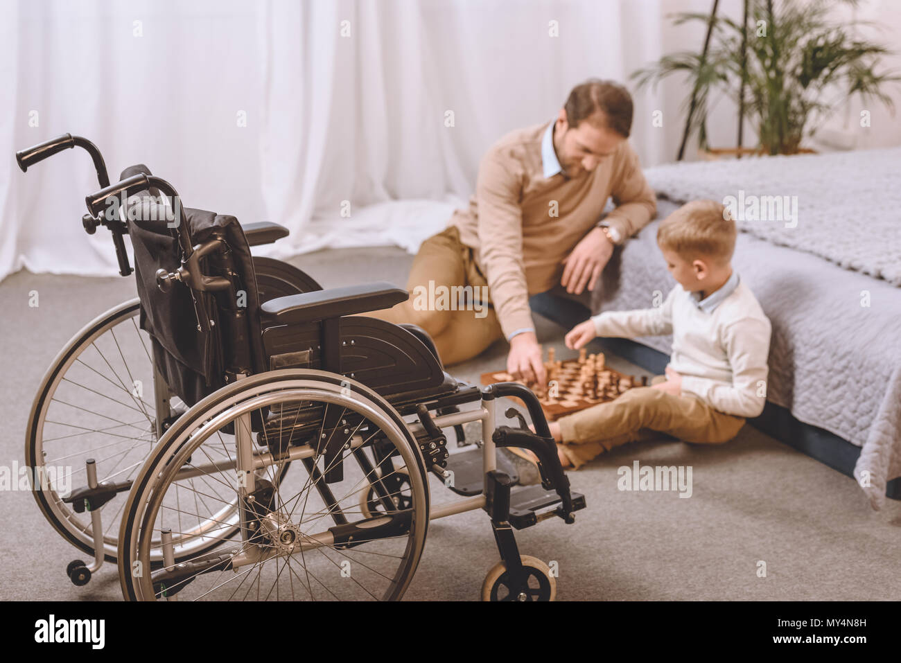 Vater und Sohn mit Behinderung spielt Schach auf einem Boden mit Rollstuhl auf Vorder Stockfoto