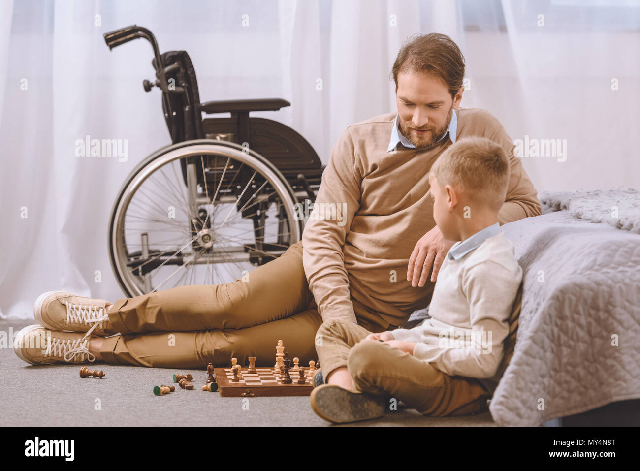 Vater und Sohn mit Behinderung spielt Schach auf einem Boden Stockfoto