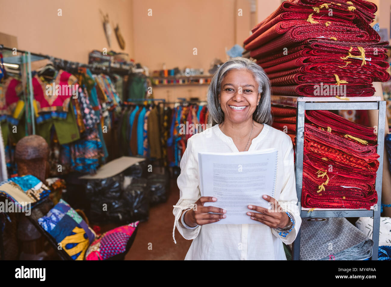 Porträt eines lächelnden reife Stoff shop besitzer lesen Papierkram beim Stehen neben Regale voll von bunten Tüchern und Textilien Stockfoto