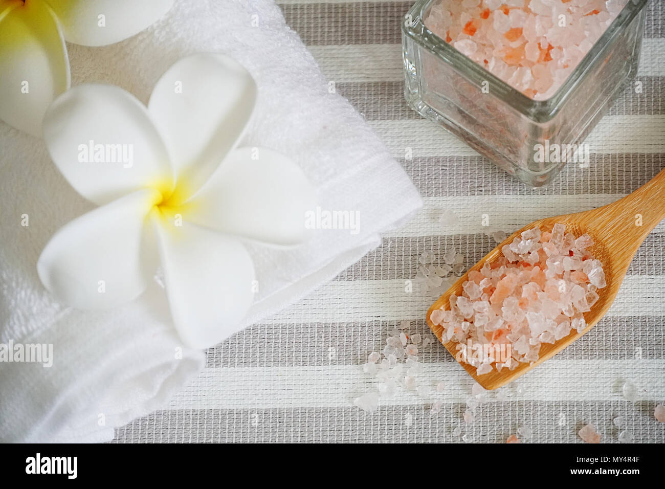Close up topview Himalaya Pink salt im Löffel und weißen Handtuch dekorieren mit weißen Blumen auf Spa-Tabelle. Stockfoto