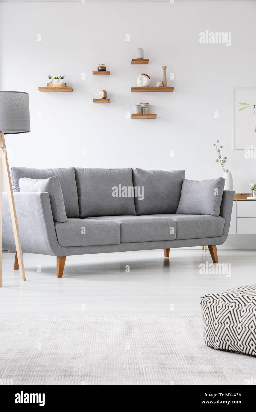 Grau couch in einfachen, hellen Wohnzimmer Interieur mit Pouf und Lampe. Real Photo Stockfoto