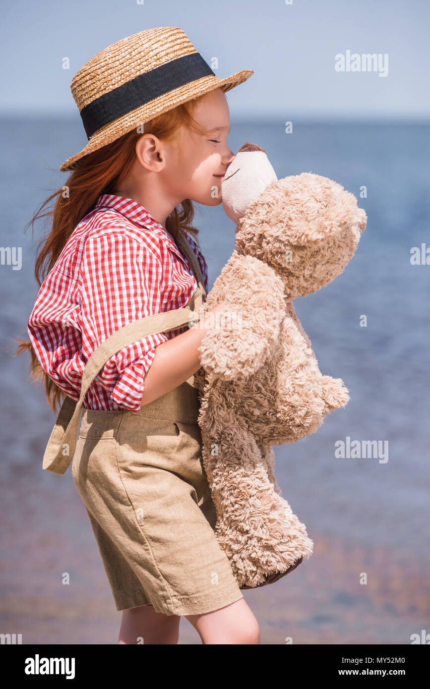 Cute glückliche kleine Mädchen mit geschlossenen Augen küssen Teddy Bär am Meer Stockfoto