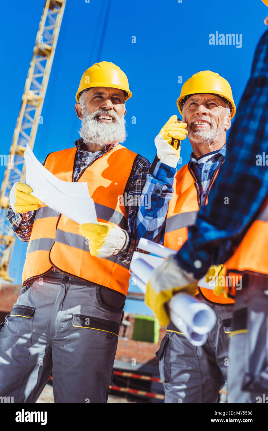 Zwei Arbeiter in hardhats und Schutzwesten auf der Baustelle mit Baupläne und tragbares Radio stehend Stockfoto