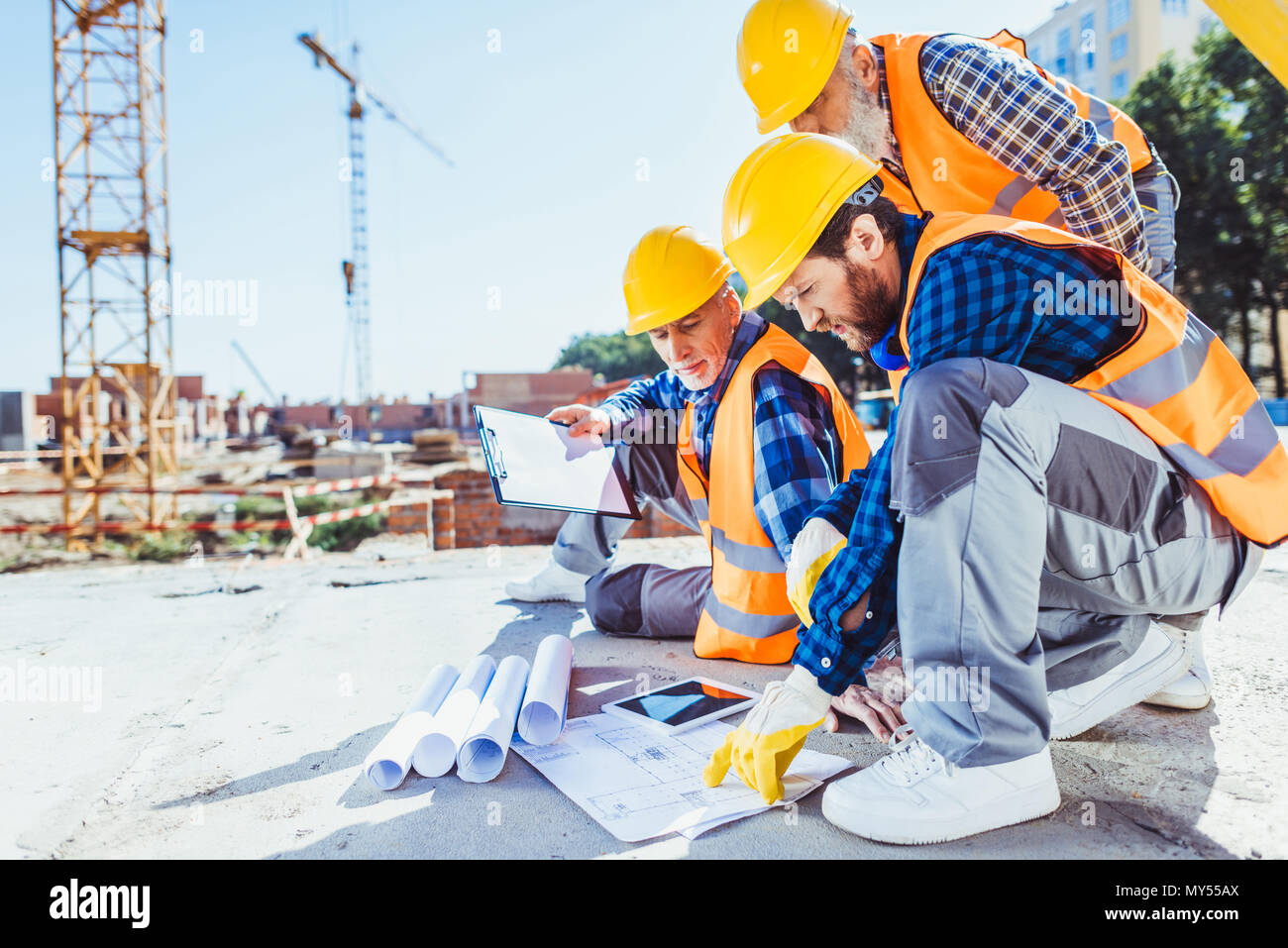 Bau Arbeiter in Uniform sitzen auf Beton auf der Baustelle, diskutieren Baupläne Stockfoto