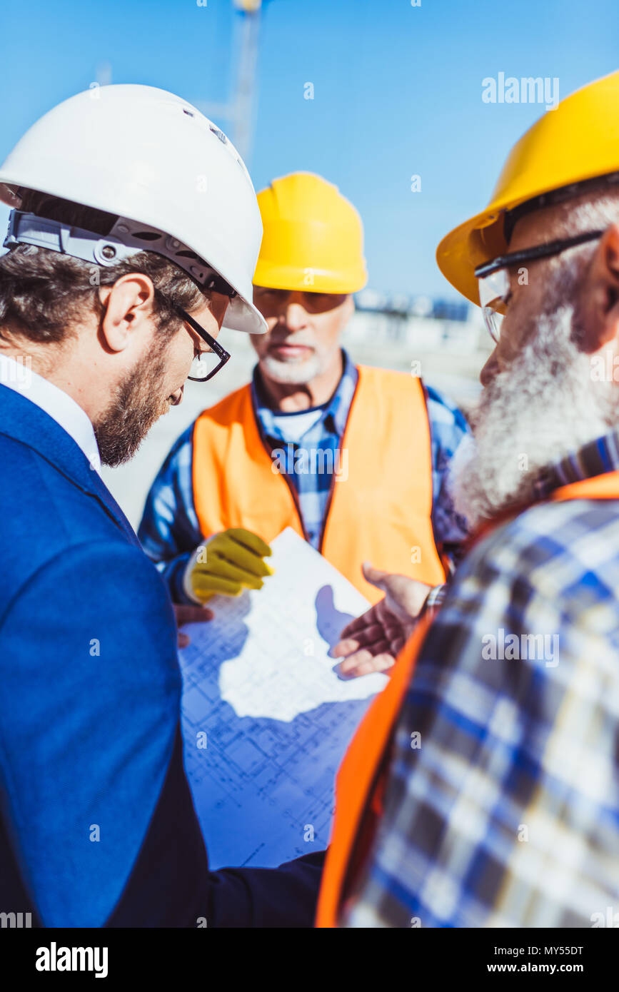 Arbeiter in Schutzkleidung uniform diskutieren Baupläne mit Geschäftsmann auf der Baustelle Stockfoto